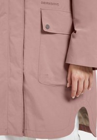 Ljusrosa vattentät jacka med en bröstficka och sidossprickor. Slät textur, minimalistisk design och subtila sömnadsdetaljer.