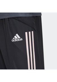 Sorte atletiske bukser med en tekstureret overflade, der har tre pink skrå striber og et broderet hvidt Adidas-logo på venstre lår.
