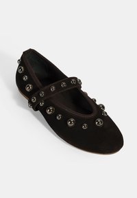 Dunkelbraune Wildlederflats mit einem Riemen, verziert mit silbernen Nieten, die entlang des Obermaterials und um die Zehen angeordnet sind, mit einer abgerundeten Form.