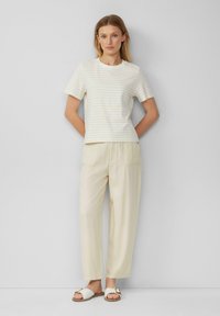 Kurzarm-T-Shirt in Weiß und Creme mit Streifen, kombiniert mit hellbeigen, weit geschnittenen Hosen und weißen Sandalen mit einer dekorativen Schnalle.