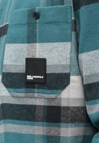 Károvaná flanelová košile v odstínech tyrkysové a šedé, s kapsou na knoflík a černou obdélníkovou nášivkou s textem "KARL LAGERFELD JEANS."