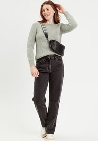 Un pull en tricot côtelé vert clair, un jean noir taille haute, des baskets blanches et un sac bandoulière noir avec une sangle rayée.