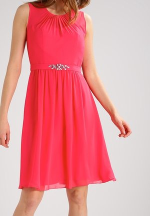 Robe rose vif sans manches, longueur genou, avec un col froncé et une ceinture décorative ornée de bijoux à la taille, portée par une personne debout.