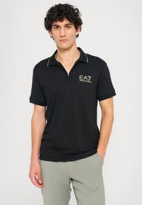 Juodas polo marškinėlis su zip užsegimu apykakle, su auksinėmis logotipo raidėmis ir akcentu. Trumpomis rankovėmis, su kontrastingu apvadu, pagamintas iš glotnios medžiagos.