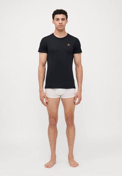 Μαύρο βαμβακερό μπλουζάκι με στρογγυλή λαιμόκοψη και μικρό κεντητό λογότυπο, συνδυασμένο με λευκά εφαρμοστά εσώρουχα. Το μοντέλο στέκεται ξυπόλητο με τα χέρια στα πλάγια.