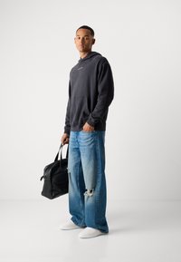 Mørkegrå oversized hoodie med frontlomme, slidte lyseblå brede jeans, hvide sneakers og en sort lædertræksæk.