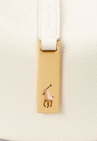 Bolso de cuero blanco texturizado con una etiqueta de hardware rectangular dorada. La etiqueta presenta un recorte del emblema de un jinete.