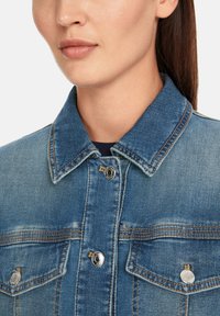 Denim jacket featuring a light blue color, classic button-up design, two chest pockets, and metal hardware accents.