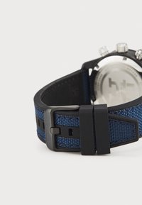 Montre de sport avec un bracelet tissé bleu marine et des accents noirs, un fermoir robuste et un boîtier en ton argent, avec des détails numériques visibles au dos.