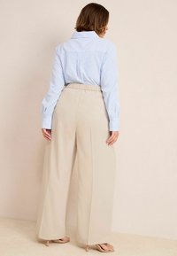 Chemise rayée bleu clair et blanche avec un col, associée �à un pantalon large taille haute beige. Tissu lisse et taille élastique.