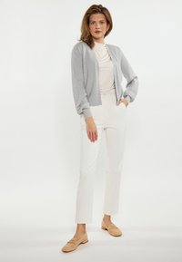 Cardigan gri deschis cu model în relief, cu mâneci evazate, asortat cu un top crem ajustat și pantaloni albi. Purtați cu loafers bej.