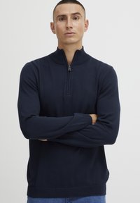 Pull en maille zippé bleu marine avec un col montant, des manches longues et des bords côtelés aux poignets et à l'ourlet. Fabriqué dans un matériau en tricot doux et texturé.