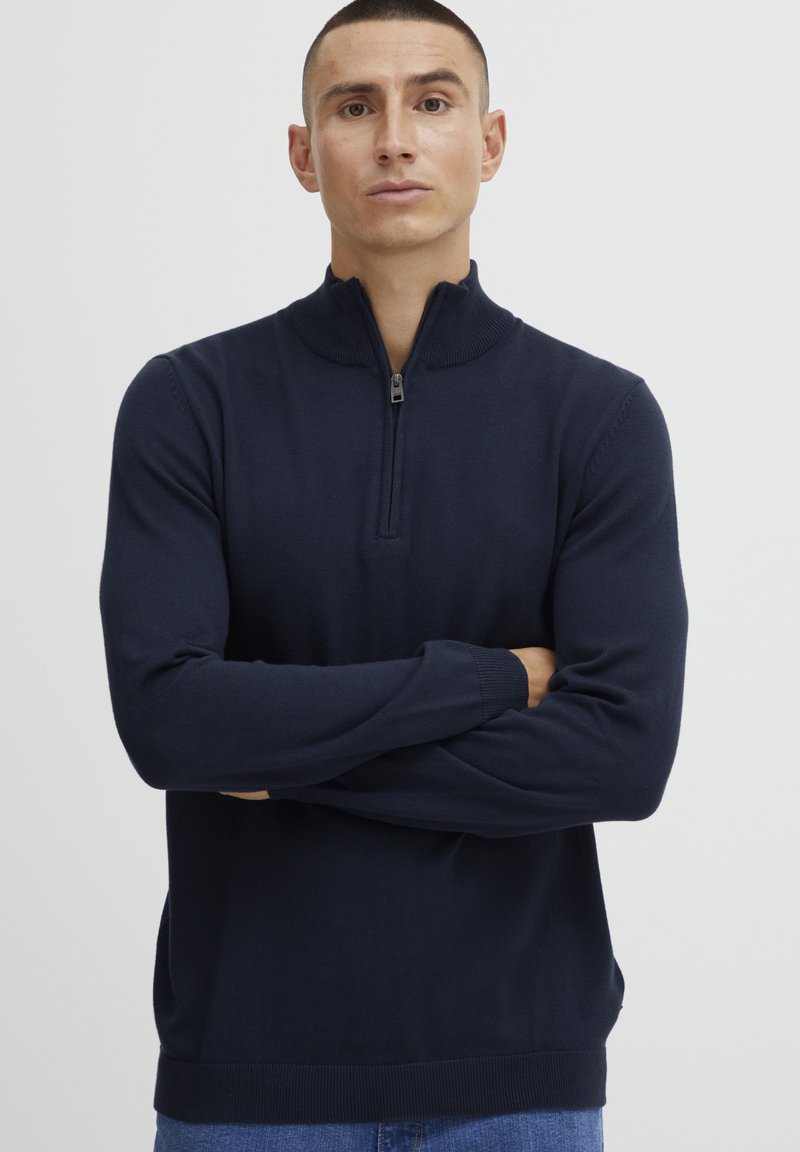 Pull en maille zippé bleu marine avec un col montant, des manches longues et des bords côtelés aux poignets et à l'ourlet. Fabriqué dans un matériau en tricot doux et texturé.