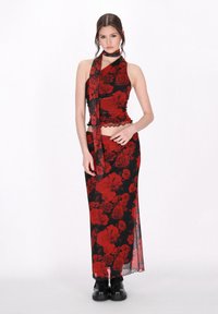 Schwarzes Kleid mit rotem Rosenmuster, tailliertes Oberteil mit Rüschensaum, Halterneck-Design, langer Rock mit einem seitlichen Schlitz, kombiniert mit schwarzen Stiefeln.