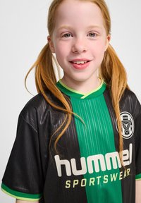 Svart och grön sporttröja med vertikala ränder, med rund halsringning, en logotyp och "hummel" i stora vita bokstäver.