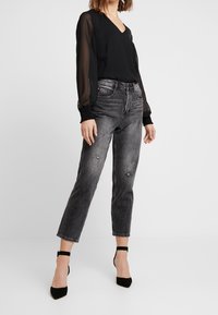 Svart, genomskinlig blus med långa ärmar och V-ringning, tillsammans med blekta grå raka jeans med slitna detaljer. Svarta klackar med ankelrem.