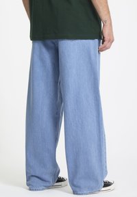 Lyseblå bredbenede jeans lavet af denim, med en ren finish og subtilt slidte detaljer. Båret med sorte sneakers.