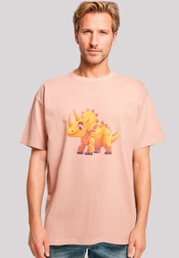 Light pink cotton t-shirt featuring a colorful cartoon triceratops graphic on the front. Loose fit with short sleeves and crew neck.