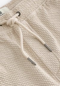 Joggers en tricot beige avec une finition texturée. Dotés d'un cordon de serrage avec des embouts métalliques argentés et d'une taille élastique pour un ajustement confortable.