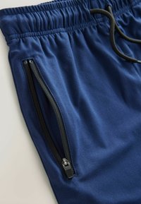 Pantalons de jogging bleu marine en tissu doux, avec une taille élastiquée, un cordon de serrage et des poches latérales zippées avec des accents noirs.