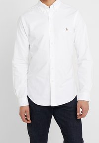 Biała koszula z długim rękawem wykonana z bawełny, z klasycznym kołnierzykiem i małym, wyszywanym logo na lewej piersi.