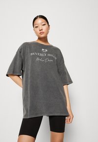 Szürke, hosszú fazonú póló, rövid ujjakkal, fehér "Beverly Hills Rodeo Drive" felirattal. Fekete kerékpáros shorttal viselve.