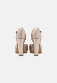 Metalické zlaté lodičky na vysokém podpatku s kulatou špičkou a velkým ozdobným prvkem vzadu, s texturovaným povrchem a mohutným podpatkem.