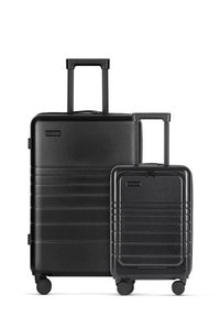 Zwart hard-shell kofferset met een horizontaal ribbelontwerp. Bevat een grote koffer en een kleinere handbagage, beide met uitschuifbare handvatten en wielen.