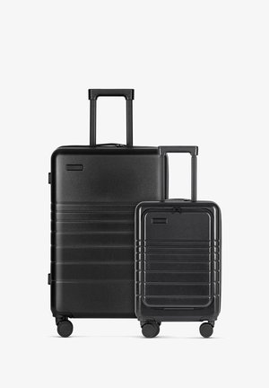 Schwarzes Hartschalengepäckset mit einem horizontalen Rippendesign. Enthält einen großen Koffer und eine kleinere Cabin-Tasche, beide mit ausziehbaren Griffen und Rollen.