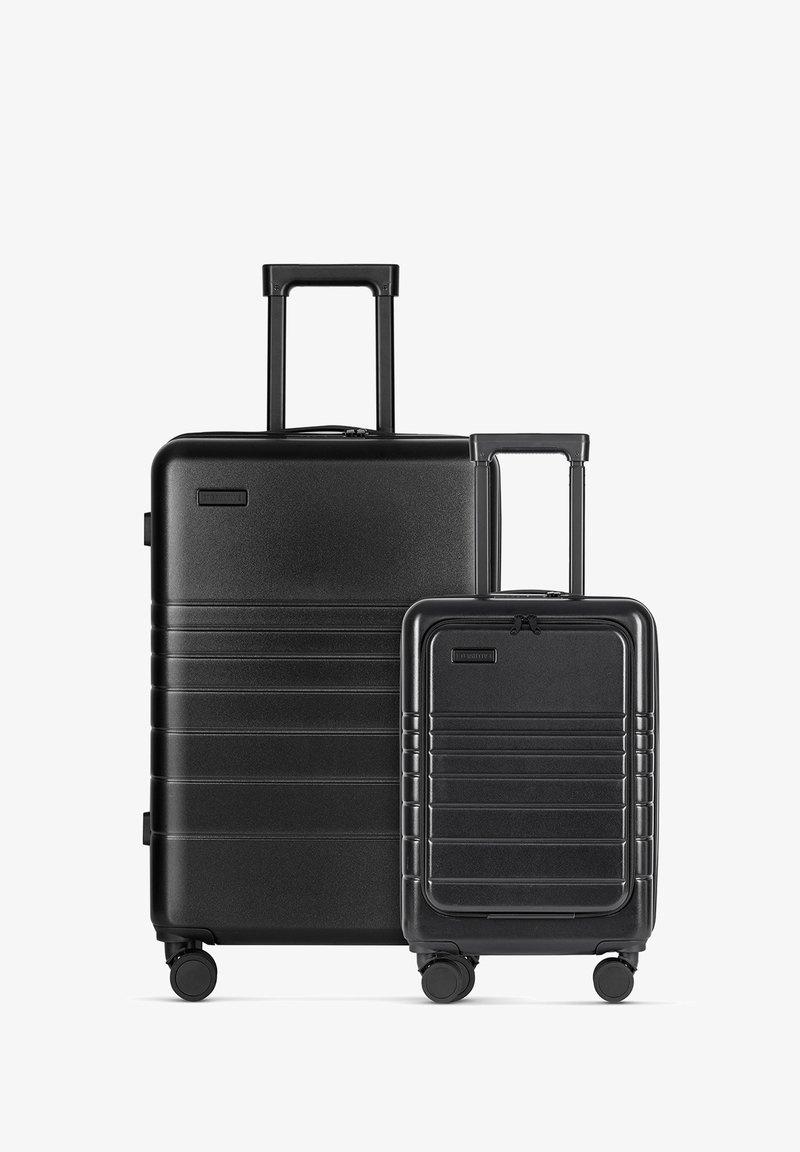 Zwart hard-shell kofferset met een horizontaal ribbelontwerp. Bevat een grote koffer en een kleinere handbagage, beide met uitschuifbare handvatten en wielen.