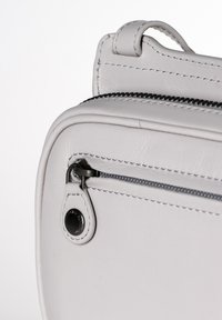 Borsa a tracolla in pelle bianca con chiusura a zip, dotata di hardware nero a contrasto, cuciture ordinate e una piccola maniglia sulla parte superiore.