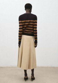 Braun und schwarz gestreifter Pullover, lange Ärmel, kombiniert mit einem knielangen beigen Rock und braunen Absätzen. Glatte Textur, lässiges Design.