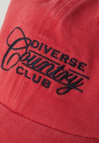 Czerwona czapka z korduroju z czarnym haftowanym napisem "DIVERSE Country CLUB". Strukturalny design z widocznymi detalami szwów.