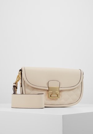 Bolso bandolera de cuero acolchado beige con correa ancha desmontable y cierre cuadrado en tono dorado sobre pedestal blanco.