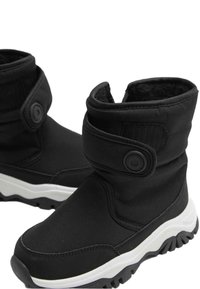 Schwarze isolierte Stiefel mit einem weichen Stoffoberteil, einem Klettverschluss und einer weißen Sohle, die ein strukturiertes Profil für den Halt aufweist.