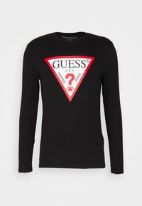 Zwart katoen shirt met lange mouwen, voorzien van een groot rood en wit driehoekig logo met de tekst "GUESS®" en "WASHED JEANS."