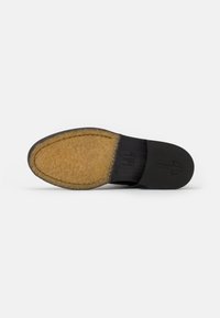 Suela de zapato de cuero negro con forro beige peludo, borde curvado y detalles en relieve. Punta plana y redondeada con superficie texturizada.