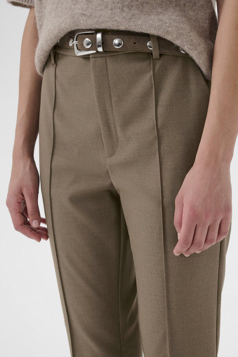 Pantalon marron sur mesure avec une texture lisse, doté d'une ceinture avec boucle argentée et de plis le long de l'avant. Mains visibles sur les côtés.