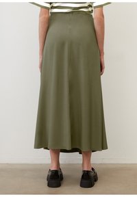 Jupe midi vert olive avec une texture lisse, une forme légèrement évasée et une couleur unie. Portée avec des chaussures noires à semelles épaisses.