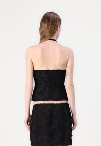 Schwarzes Top mit Halterneck aus strukturiertem Material, das eine figurnahe Passform und fransige Kanten aufweist. Der Rücken ist glatt mit einem schlichten Schnitt.
