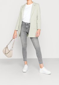 Jasnozielona marynarka na białej koszulce, zestawiona z szarymi wąskimi dżinsami, białymi sneakersami na platformie oraz beżową torebką z łańcuszkiem.
