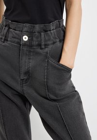 Pantalones de mezclilla negros con un diseño de cintura alta, que cuentan con bolsillos laterales y un detalle de botón visible en la cintura. Textura suave.