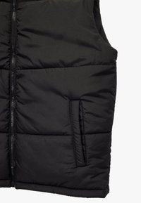 Sort polstret vest med lynlås, sidelomme, glat tekstur og vandret syning for isolering. Ærmeløs for nem bevægelse.