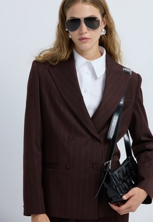 Bordeaux dubbelgeknopte pinstriped blazer, wit overhemd met kraag, zilveren aviator zonnebril en een kleine zwarte geweven handtas.