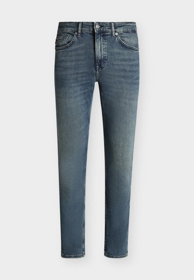 Jean slim bleu délavé avec cinq poches et une fermeture par bouton et zip sur un fond uni.
