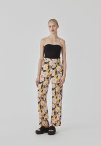 Top negro sin tirantes combinado con pantalones de pierna ancha de cintura alta con un estampado floral en rosa, amarillo y azul sobre un fondo negro.