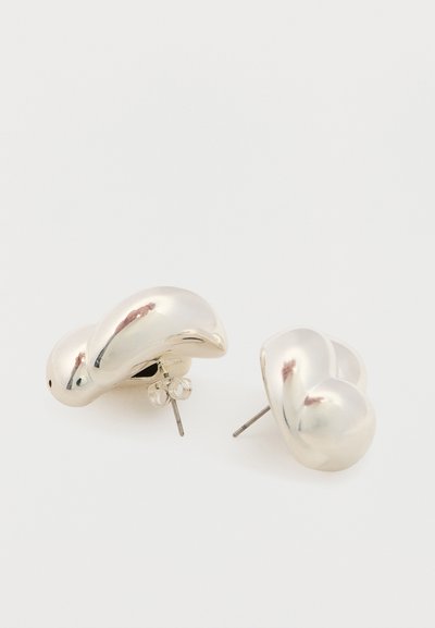 Orecchini a perno in metallo color argento massiccio con una forma curva organica astratta e chiusure a farfalla su sfondo bianco.