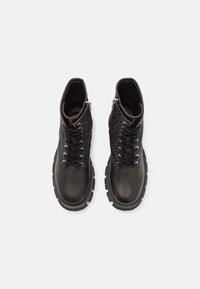 Bottines noires avec un dessus en cuir lisse, des accents en tissu texturé, un laçage à l'avant avec des éléments en métal argenté, et des semelles en caoutchouc robustes.
