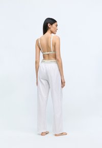 Pajama hlače Calvin Klein s črtami in širokimi nogavicami. Lahek material z bež pasom. Braletka z tankimi naramnicami, zadnji pogled.