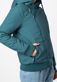 Tyrkysová kapucová bunda se zipem vpředu, bočními kapsami a žebrovanými manžetami. Hladký povrch s minimalistickým designem a bez viditelných vzorů.